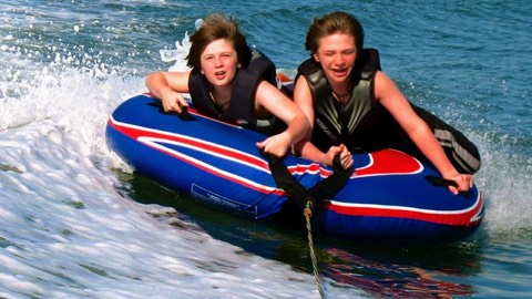 Kids surf wave while tubing behind boat